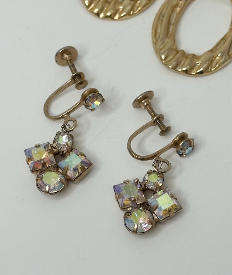 May include: A pair of gold tone clip-on earrings with iridescent stones. The earrings have a cluster of stones in the shape of a flower.