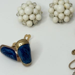 May include: A set of four vintage clip-on earrings. Two pairs of earrings feature white beads and clear rhinestones. The other pair features blue enamel with gold accents.