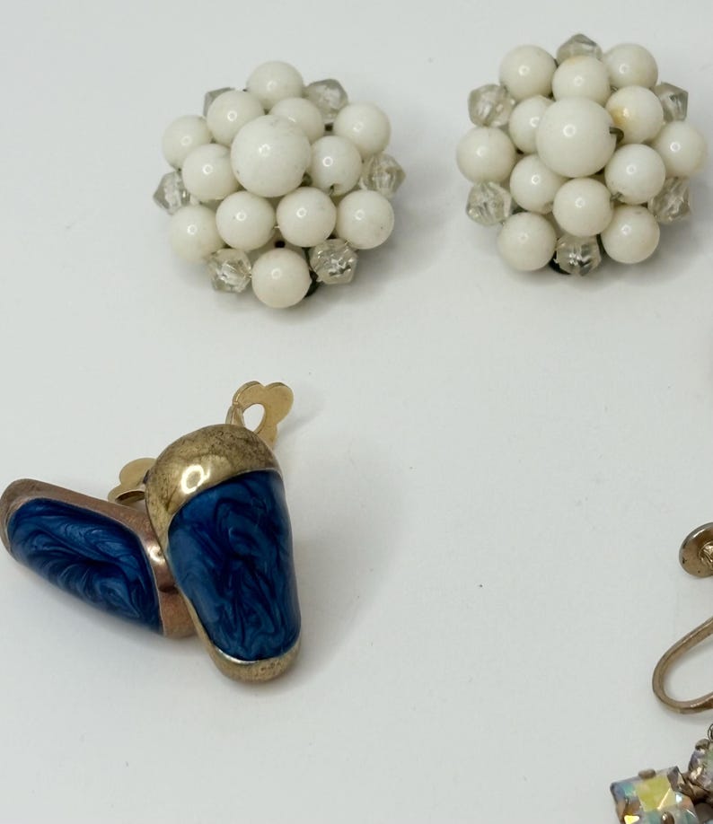 May include: A set of four vintage clip-on earrings. Two pairs of earrings feature white beads and clear rhinestones. The other pair features blue enamel with gold accents.