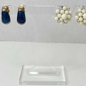 May include: Two pairs of earrings on a display stand. One pair is blue with a swirl pattern and the other pair is white and round.