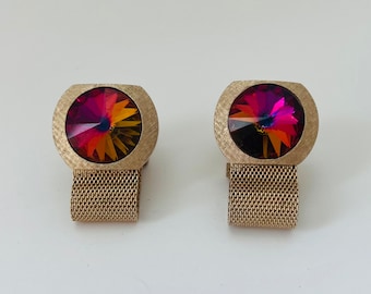May include: A pair of gold cufflinks with a round, iridescent red, orange, and yellow gemstone in the center of each cufflink. The cufflinks have a mesh band.