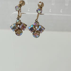 May include: A pair of gold tone clip-on earrings with iridescent purple and pink stones. The earrings have a cluster of stones in the shape of a flower.