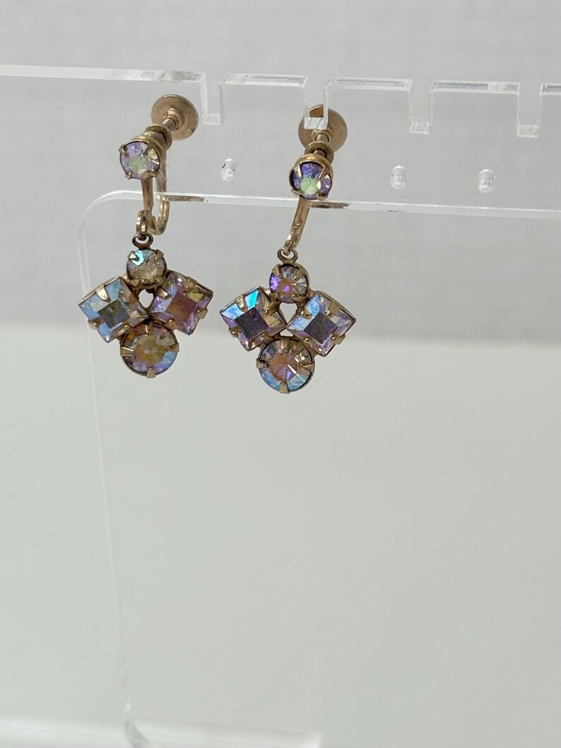 May include: A pair of gold tone clip-on earrings with iridescent purple and pink stones. The earrings have a cluster of stones in the shape of a flower.