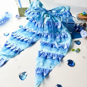 May include: A large blue and light blue bow with multiple layers of ruffles and rhinestones. The bow is tied in a large knot and has long tails.