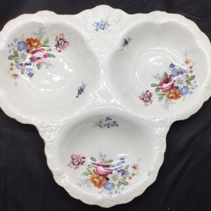 May include: A white porcelain serving dish with three sections, each decorated with a floral pattern in shades of pink, red, blue, and yellow. The dish has a gold rim and a scalloped edge.