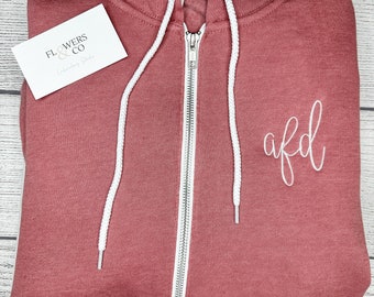 May include: A pink zip-up hoodie with white drawstrings and a white embroidered design that says "afd".