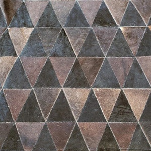 K&ouml;nnte beinhalten: Ein brauner und schwarzer Patchwork-Teppich aus Leder mit einem geometrischen Muster aus Dreiecken.
