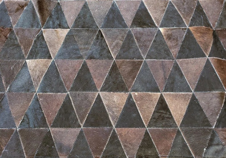 K&ouml;nnte beinhalten: Ein brauner und schwarzer Patchwork-Teppich aus Leder mit einem geometrischen Muster aus Dreiecken.