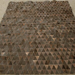 K&ouml;nnte beinhalten: Ein brauner und schwarzer geometrischer Teppich aus Lederdreiecken. Der Teppich hat einen dezenten Glanz und liegt flach auf einer grauen Oberfl&auml;che.