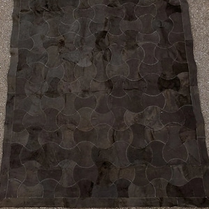 K&ouml;nnte beinhalten: Ein schwarzer Lederteppich mit einem geometrischen Muster aus &uuml;berlappenden Kreisen. Der Teppich hat einen dunkelbraunen Rand.