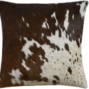 May include: Brown and white cowhide cushion with a natural, spotted pattern. The cushion is made from real cowhide and has a soft, luxurious feel.