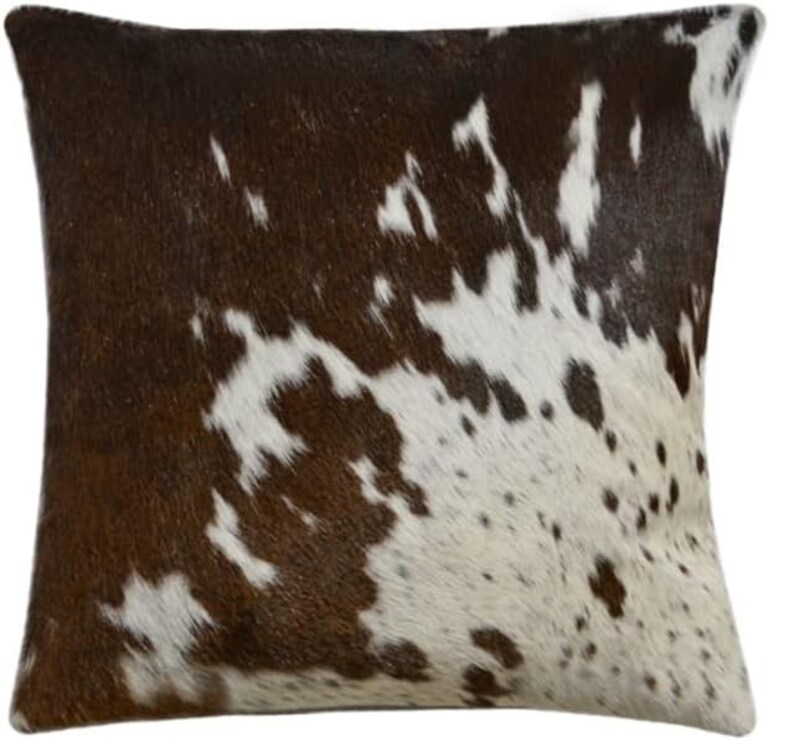 May include: Brown and white cowhide cushion with a natural, spotted pattern. The cushion is made from real cowhide and has a soft, luxurious feel.