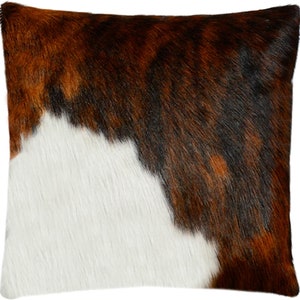 May include: A brown, white and black cowhide throw pillow with a soft, fuzzy texture.