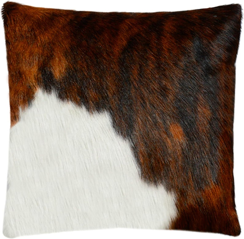 May include: A brown, white and black cowhide throw pillow with a soft, fuzzy texture.