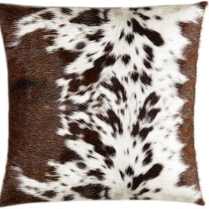May include: A brown and white cowhide cushion with a natural, spotted pattern. The cushion is soft and plush, ideal for adding a touch of rustic charm to any room.