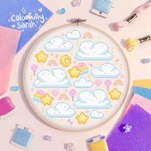Peut inclure: Un cercle de broderie rond avec un fond blanc et un motif de point de croix coloré représentant des nuages, des étoiles, des arcs-en-ciel et des bonbons. Le motif est entouré d'un cerceau en bois.