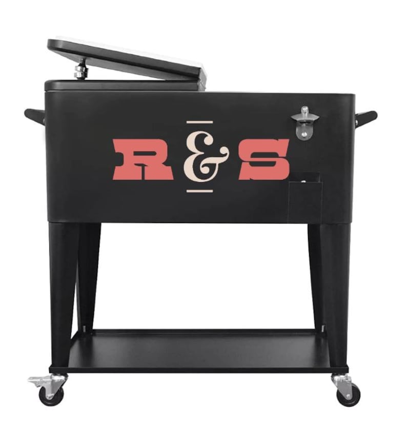 May include: Black metal cooler with the letters "R & S" in red and white. The cooler has a hinged lid, a bottle opener, and sits on a black metal stand with wheels. The cooler is designed for outdoor use.