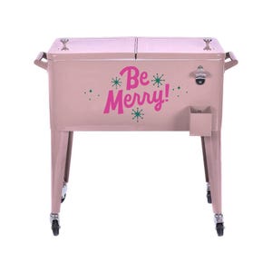 May include: A pink metal cooler with the words "Be Merry!" in magenta. The cooler has a bottle opener, a small storage compartment, and is on wheels. It has handles on each side.
