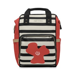 May include: A red, black, and cream striped backpack with a large red flower graphic on the front. The backpack has a black handle and the text "sugar monsters." The sides are red with tan pockets and gold zippers.
