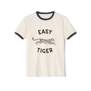 May include: A white t-shirt with a navy blue ringer. The shirt has a black graphic of a cheetah running with the text "EASY TIGER" underneath.