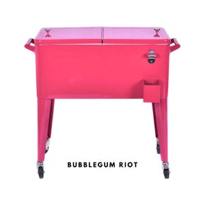 May include: A bubblegum pink metal cooler with a dual-lid design, handles, and a bottle opener. The cooler has a small storage compartment and sits on four caster wheels. The text "BUBBLEGUM RIOT" is printed on the front.