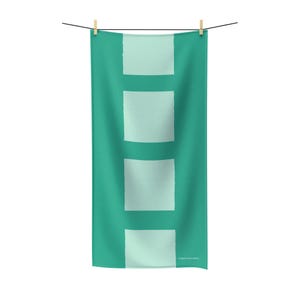 May include: A teal beach towel with four light teal rectangular blocks. The towel is hanging from a clothesline with two wooden clothespins. The words "sugar monsters" are printed at the bottom right corner.