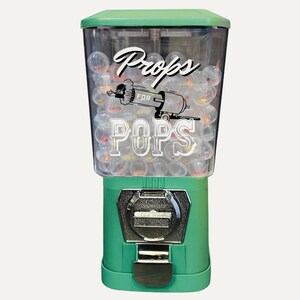 May include: A green gumball machine with a clear plastic top filled with small, colorful gumballs. The machine has a silver coin slot and a dispenser. The words "Props for Pops" are printed on the front.