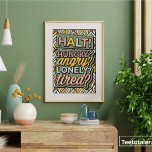 May include: A framed print with a green, yellow, and pink geometric pattern. The print features the text "HALT! HUNGRY? angry? LONELY? tired?" in a bold, colorful font.