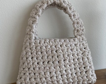 May include: A small, beige crocheted handbag with a single handle. The bag is made with a sparkly yarn.