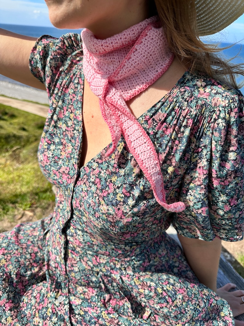 May include: A woman wearing a floral dress with a pink crocheted scarf around her neck.