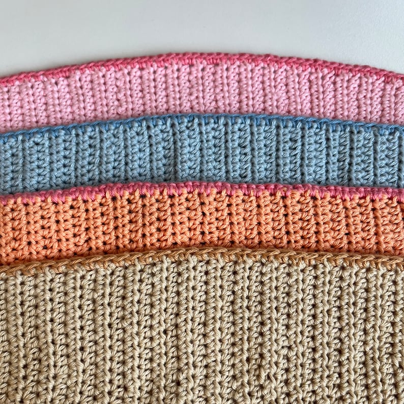 May include: Four crocheted fabric strips in different colors: beige, peach, light blue, and pink. The strips are stacked on top of each other, with the beige strip at the bottom and the pink strip at the top.