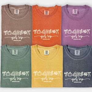May include: Six t-shirts in various colors: espresso, orange, purple, green, yellow, and gray. Each shirt features a white graphic with a pumpkin, coffee cup, leaves, and the text "girls trip, Vermont 2025."