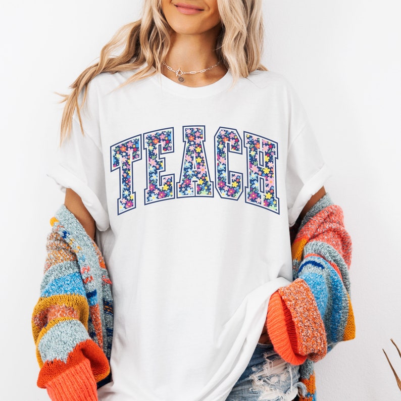 May include: White t-shirt with the word "TEACH" in blue outlined letters filled with a floral pattern.