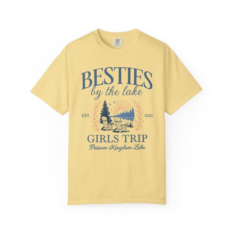 K&ouml;nnte beinhalten: Hellgelbes T-Shirt mit dem marineblauen Schriftzug "BESTIES by the lake". Darunter eine See-Szene mit St&uuml;hlen und B&auml;umen sowie dem Text "GIRLS TRIP Possum Kingdom Lake". Das Shirt hat auch den Aufdruck "EST. 2025".