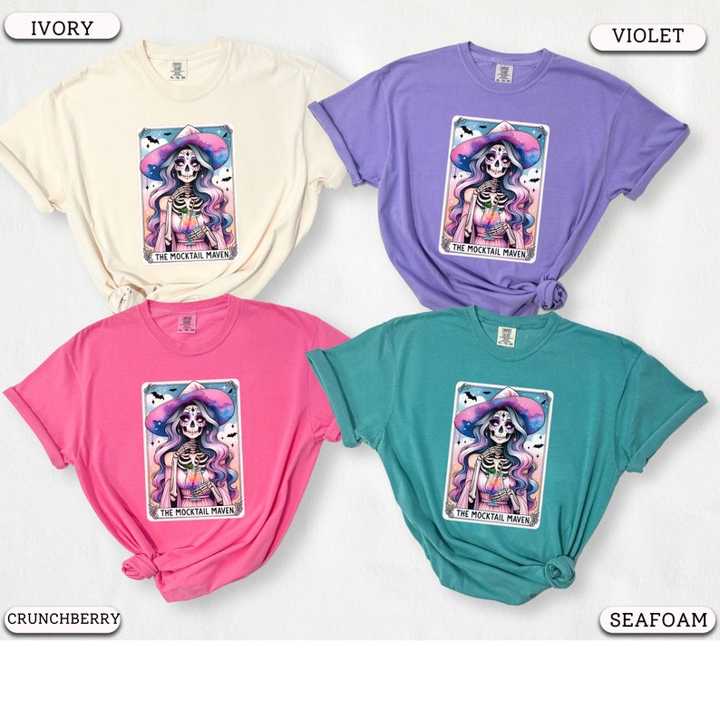 May include: Four different colored t-shirts featuring a colorful illustration of a skeleton wearing a witch's hat and holding a glass of liquid. The text "The Mocktail Maven" is printed below the illustration.