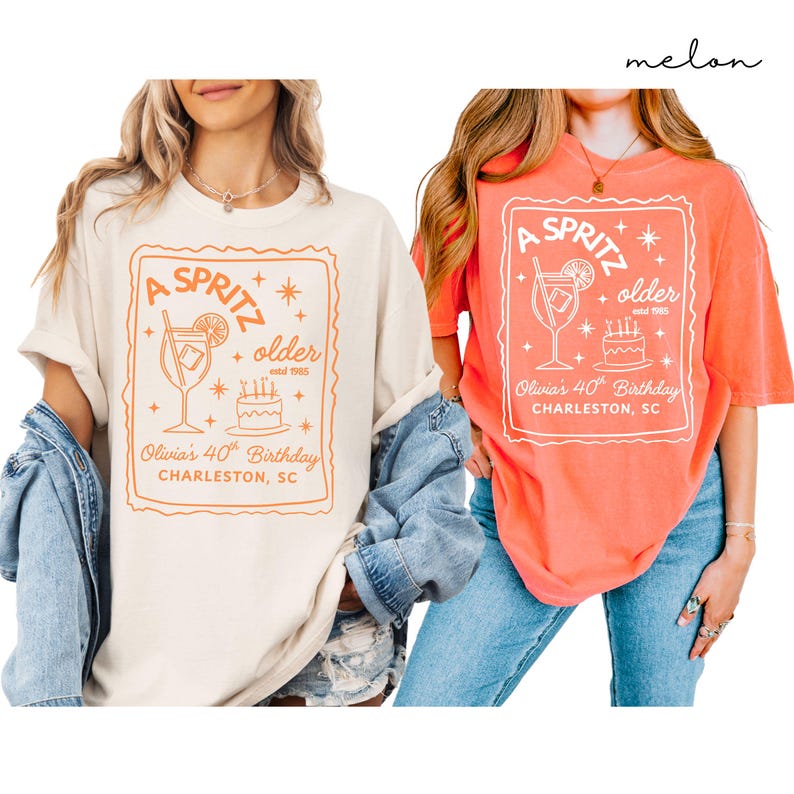 May include: Two t-shirts, one cream and one coral, with a graphic design. The design features the text "A Spritz Older" with a cocktail illustration, a cake, and the text "Olivia's 40th Birthday, Charleston, SC."