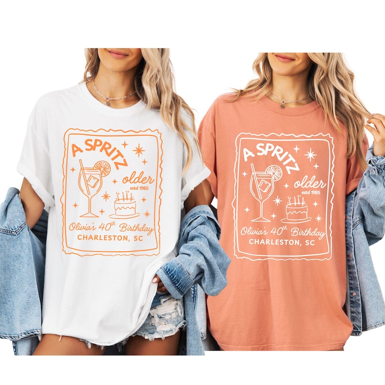 May include: Two t-shirts, one white and one coral, each featuring a rectangular design with the words "A Spritz" and "older estd 1985." The design includes a cocktail glass, a cake, and the text "Olivia's 40th Birthday, Charleston, SC."