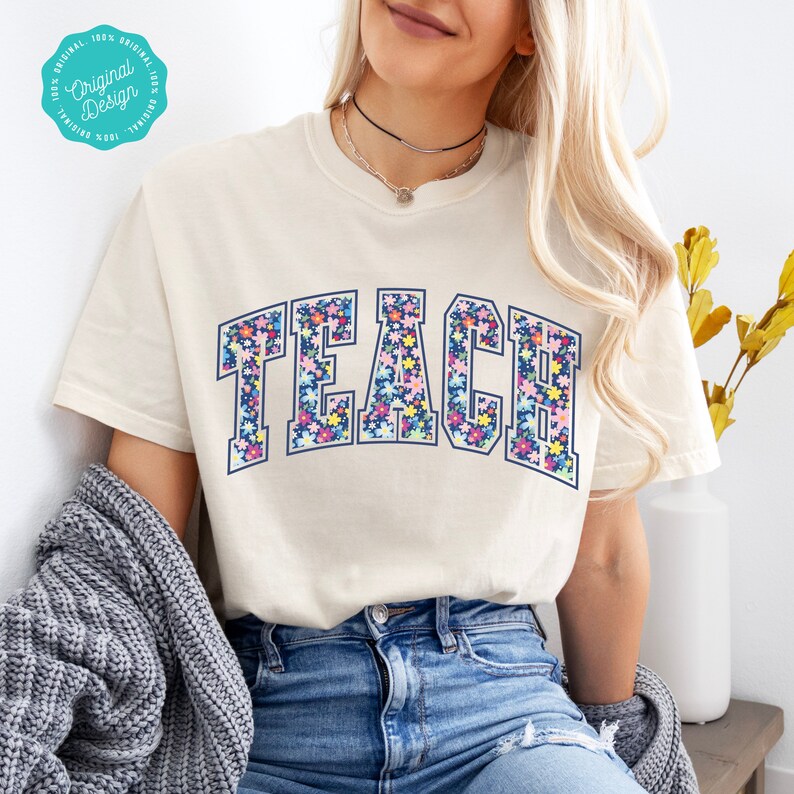 May include: A white t-shirt with a floral print of the word "TEACH" in navy blue letters with a light blue outline.