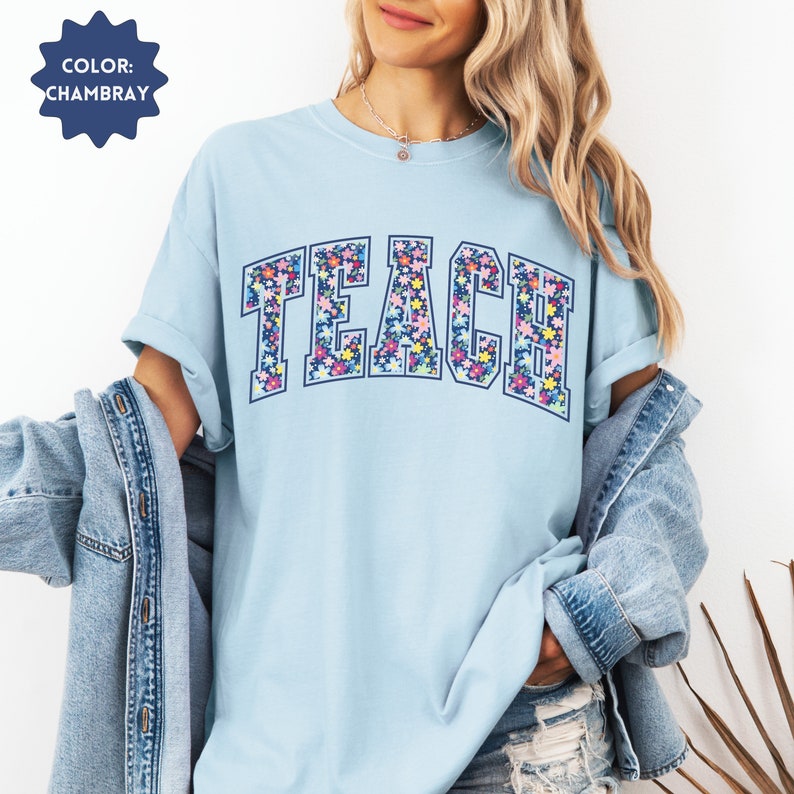 May include: A light blue t-shirt with the word "TEACH" in large, navy blue letters. The letters are filled with a colorful floral pattern.