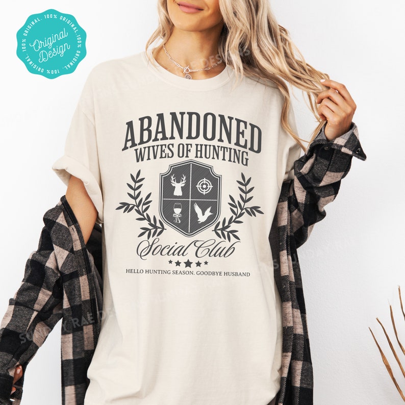 May include: A beige t-shirt with a black graphic that says "Abandoned Wives of Hunting Social Club" with a hunting-themed crest and the text "Hello Hunting Season, Goodbye Husband".