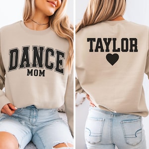 May include: Beige sweatshirt with the text "DANCE MOM" in black block letters on the front. The back of the sweatshirt has the name "TAYLOR" in black block letters with a black heart below.