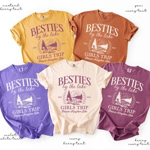 K&ouml;nnte beinhalten: F&uuml;nf T-Shirts in Senf-, Yam-, Violett-, Elfenbein- und Beerent&ouml;nen. Jedes Shirt zeigt den Text "BESTIES by the lake" mit einer Seeufer-Grafik und den Worten "GIRLS TRIP".