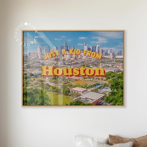 Könnte beinhalten: Ein gerahmter Druck mit einer Stadtlandschaft von Houston unter blauem Himmel. Der Druck trägt den Text "JUST A KID FROM Houston" in gelben und roten Buchstaben. Der Druck wird über einer Holzbank mit Kissen und einer Decke angezeigt.