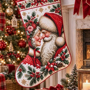 Puede incluir: Un calcetín navideño con un diseño detallado de punto de cruz de Santa Claus y la Señora Claus frente a frente. El calcetín está decorado con bayas rojas, hojas de acebo verdes, flores de pascua y copos de nieve dorados sobre un fondo crema.