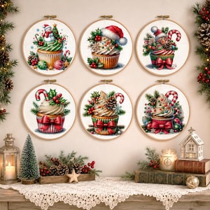 Könnte beinhalten: Sechs kreisförmige Stickrahmen mit festlichen Cupcake-Illustrationen. Jeder Cupcake ist mit weihnachtlichen Elementen wie Zuckerstangen, Tannenzapfen, Stechpalmen, Schneemännern und Weihnachtsmützen auf hellem Stoff verziert.