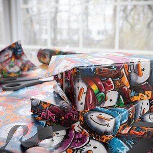May include: A stack of colorful wrapping paper featuring a snowman design. The paper is printed with a variety of colors, including red, blue, green, yellow, and white. The snowman is depicted in a cartoon style with a black hat, a carrot nose, and a black scarf.