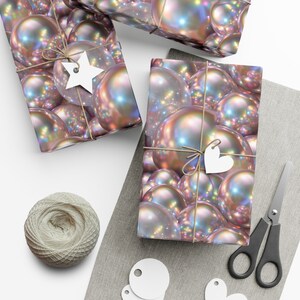 May include: Three gift boxes wrapped in iridescent pearl-like wrapping paper with brown twine and white paper tags. The boxes are on a light gray surface with a spool of twine, scissors, and white paper circles.