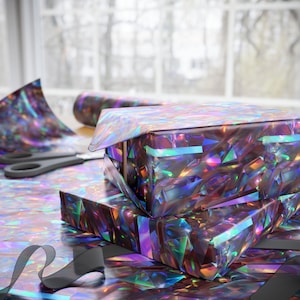 May include: Two iridescent gift boxes wrapped in holographic wrapping paper with a rainbow sheen. The boxes are stacked on top of each other and are surrounded by more wrapping paper.