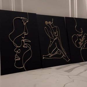 May include: Three black canvas art pieces with gold wire line art depicting human figures and faces. The art pieces are displayed against a white wall and a marble floor. The Instagram handle "art_in_interior_minsk" is visible in the bottom left corner.