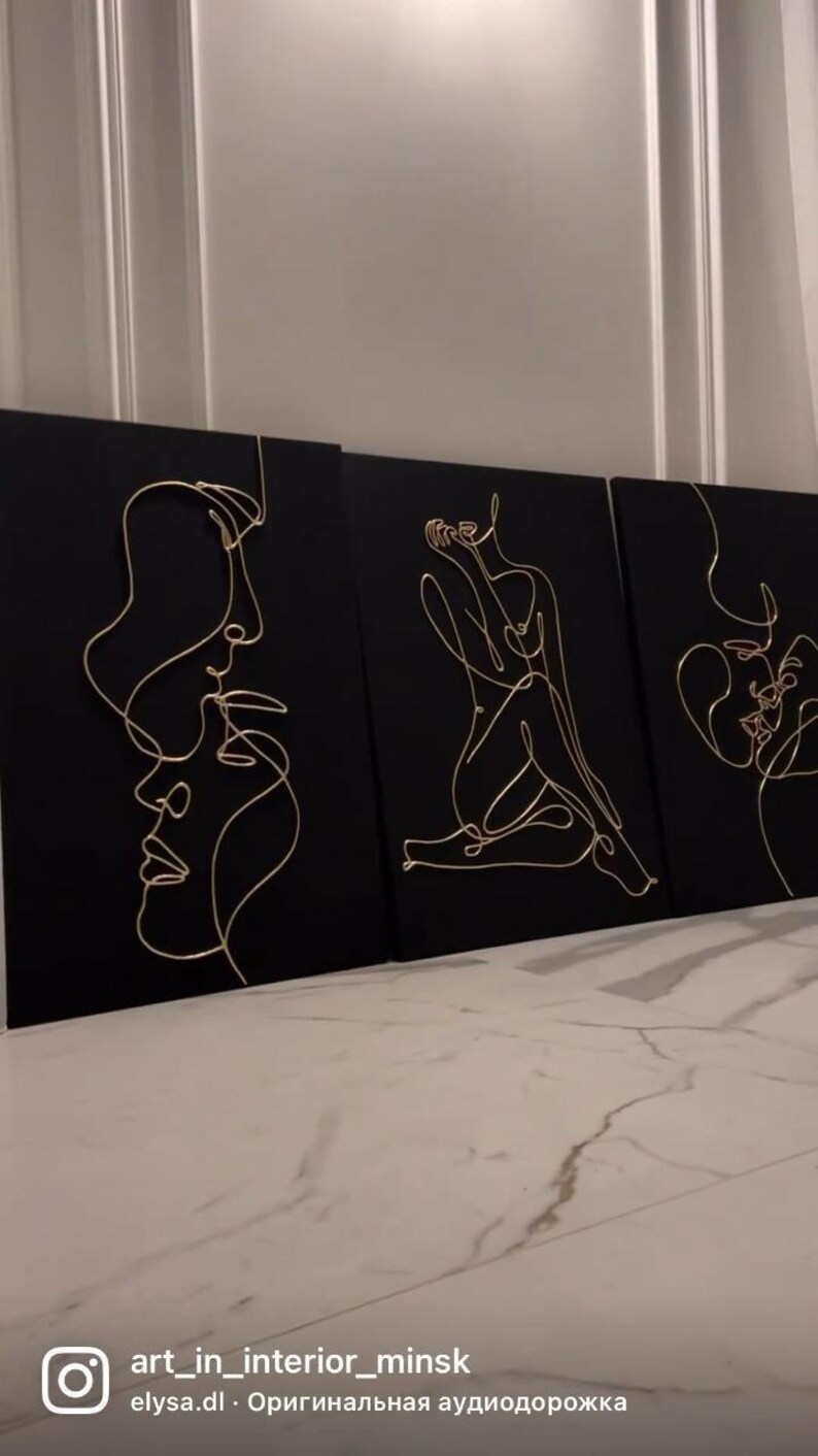 May include: Three black canvas art pieces with gold wire line art depicting human figures and faces. The art pieces are displayed against a white wall and a marble floor. The Instagram handle "art_in_interior_minsk" is visible in the bottom left corner.